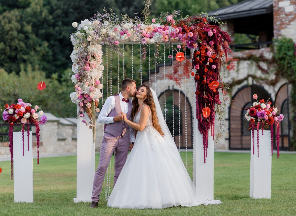 A wedding couple standing under a floral archway before the ceremony